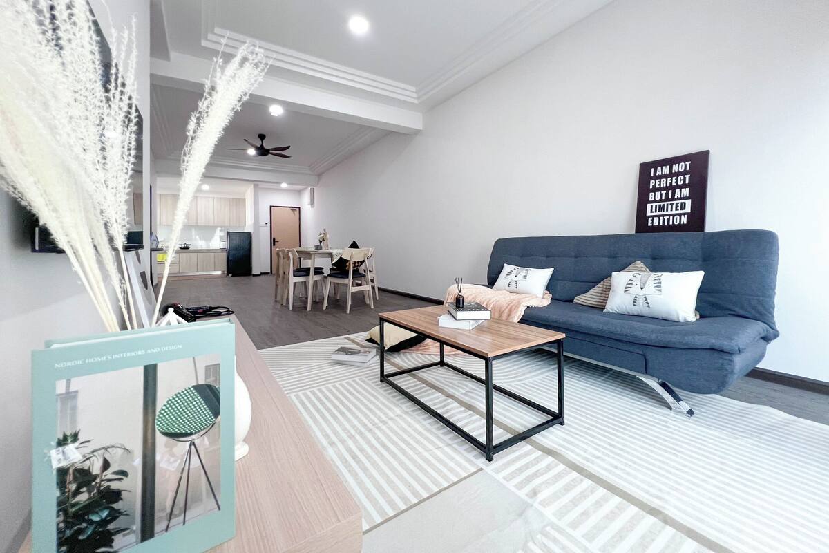 A modern living room with a blue sofa, a coffee table, and a dining area in the background.