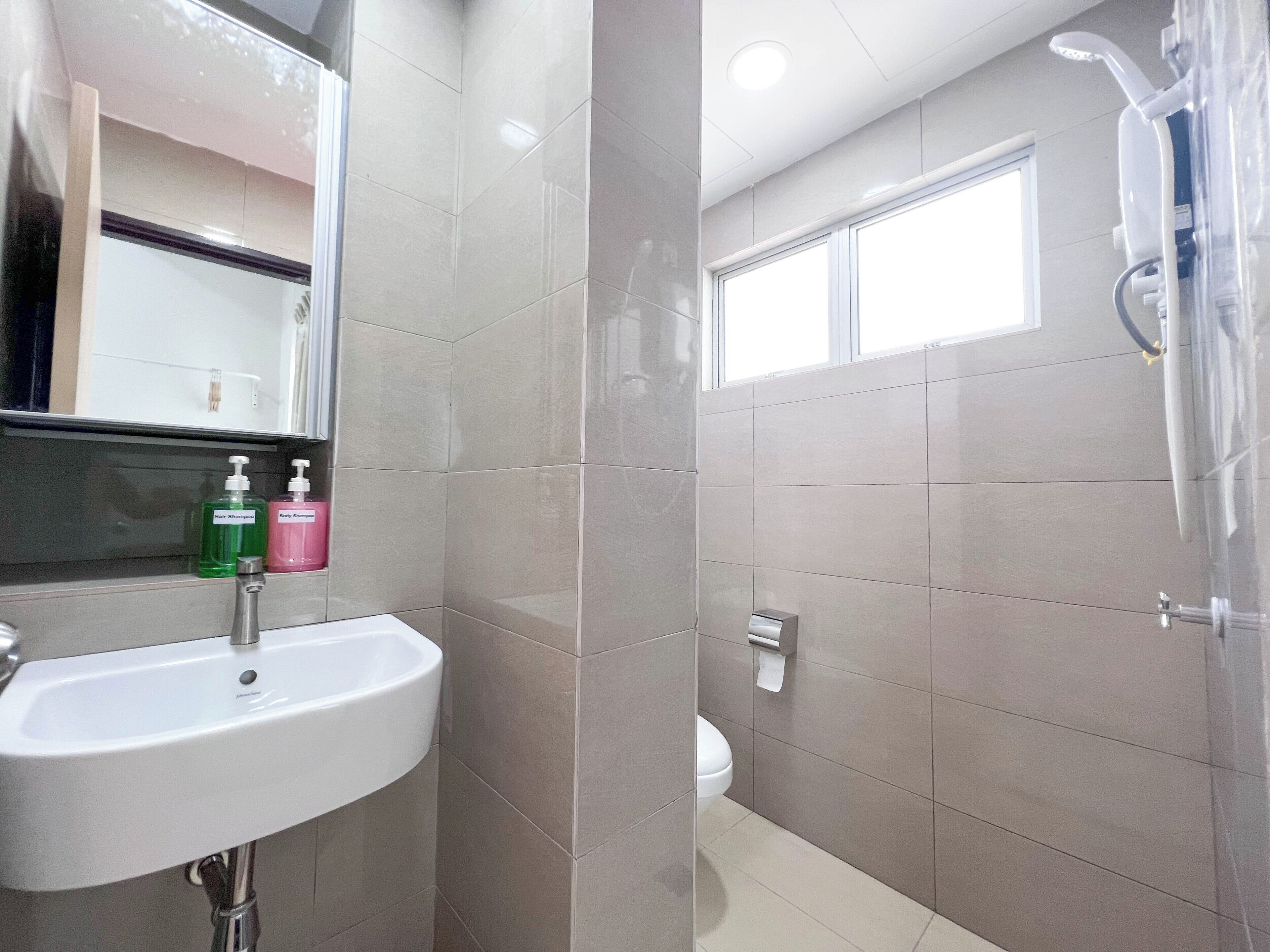 A modern bathroom with a white sink, two bottles of shampoo, a toilet, and a shower.