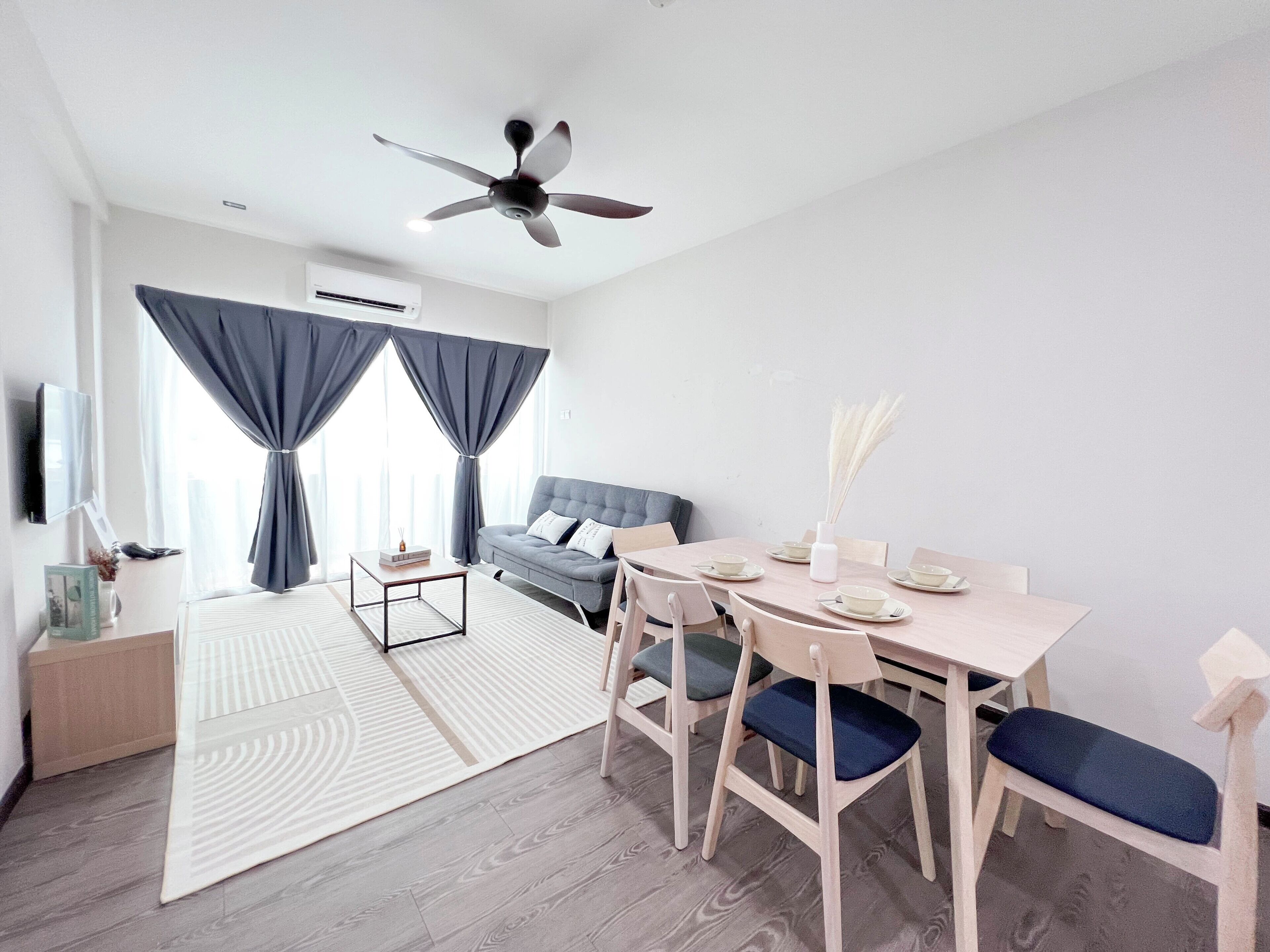 A modern living room with a sofa, dining table, and chairs. There is a ceiling fan and an air conditioning unit.