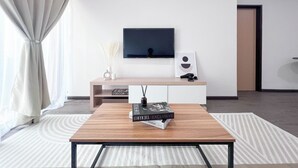 A modern living room with a wooden coffee table, a flat-screen TV mounted on the wall, a minimalist console table, and a large window with sheer curtains. - MH Maison by Manhattan Group  (Kuala Lumpur)