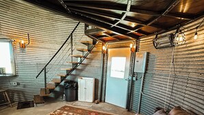 A rustic interior with a leather couch, patterned rug, and a staircase leading to a loft area. - UNIQUE Grainbin Ranch Stay (Johnson City)