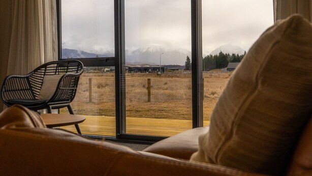 A room with a large window offering a view of a mountainous landscape. - Tussock Bend Horizons (Twizel)