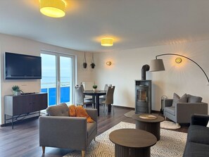 A modern living room with a flat-screen TV, a dining area, a fireplace, and a sofa.