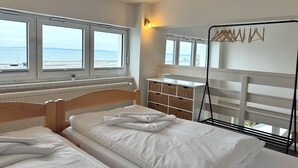 Ett hotellrum med en säng, ett skrivbord, en stol, ett element och utsikt över havet.