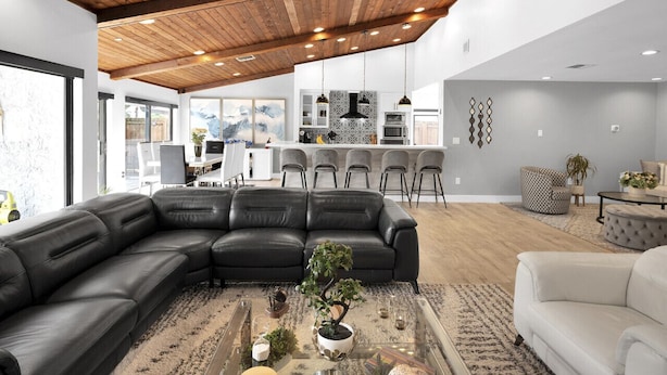Un salon moderne avec un grand canapé d’angle, une table basse agrémentée d’objets décoratifs et, au fond, un espace cuisine.