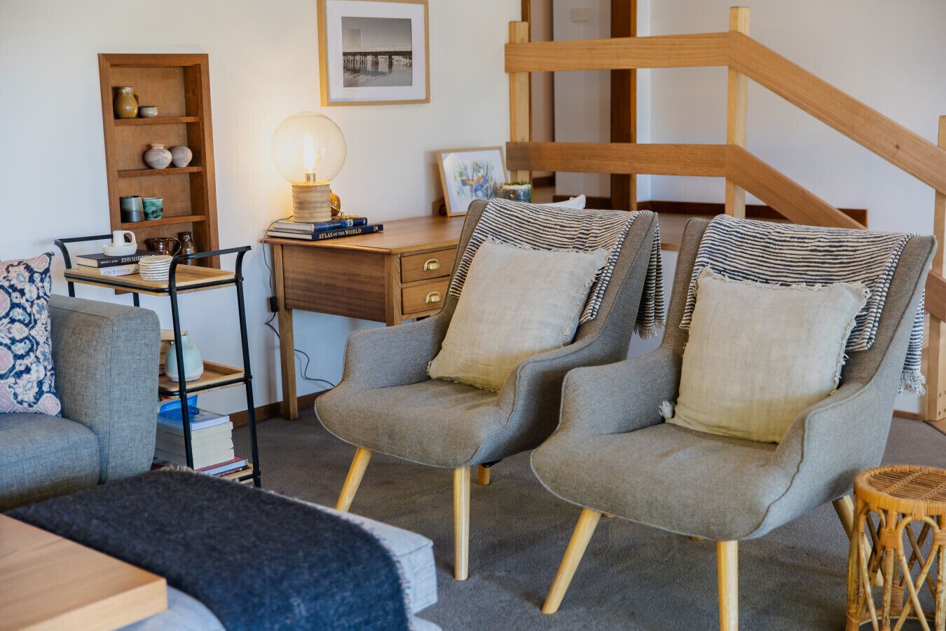 A cozy living room with a wooden staircase, a desk with books, and a lamp.