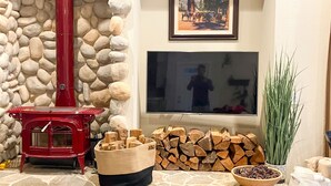 A fireplace with a red chimney, a TV mounted on the wall, a framed painting, and a stack of firewood.