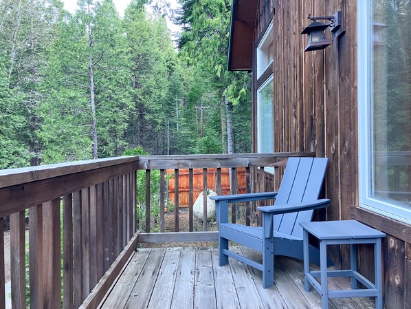 A wooden deck with two blue Adirondack chairs and a small table.