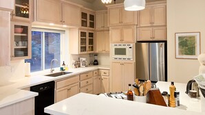 A modern kitchen with light wood cabinets, a stainless steel refrigerator, a microwave, and a coffee maker.