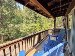 Une terrasse en bois avec des chaises Adirondack bleues donnant sur une zone boisée.