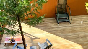 A wooden deck with two lounge chairs and a small table, a metal staircase, and a tree.