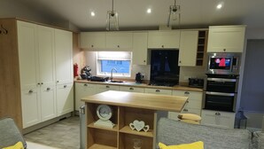 Una cocina moderna con armarios blancos, encimera de madera y horno integrado. Hay una ventana que proporciona luz natural, y un televisor montado sobre el horno.