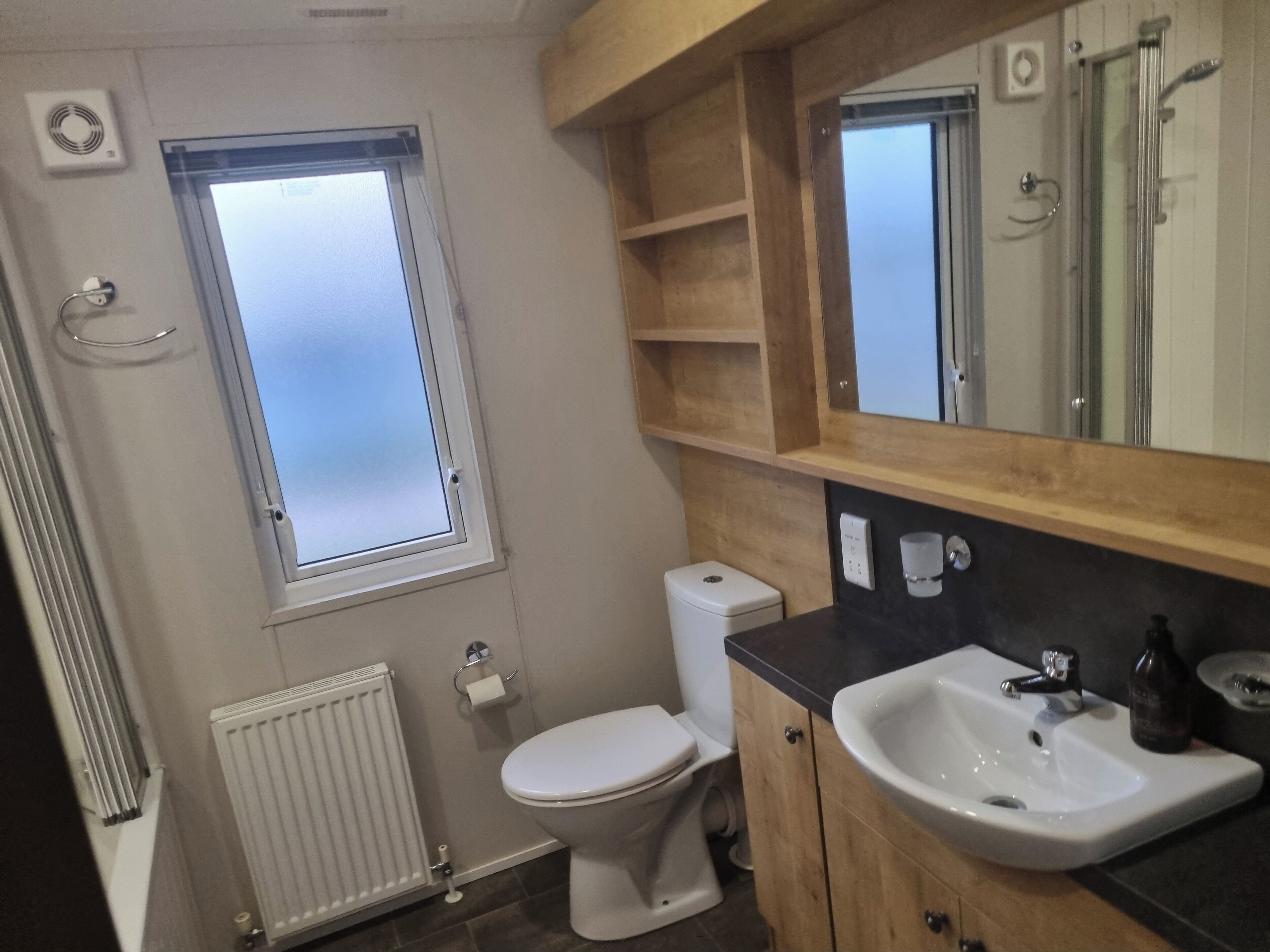 Een badkamer met toilet, wastafel, spiegel en raam.