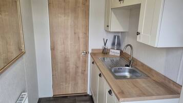 Een kleine keuken met een houten deur, een spoelbak en witte keukenkastjes.