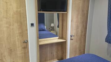Een slaapkamer met een bed, een aan een houten wand bevestigde televisie en een klein nachtkastje met een lamp.