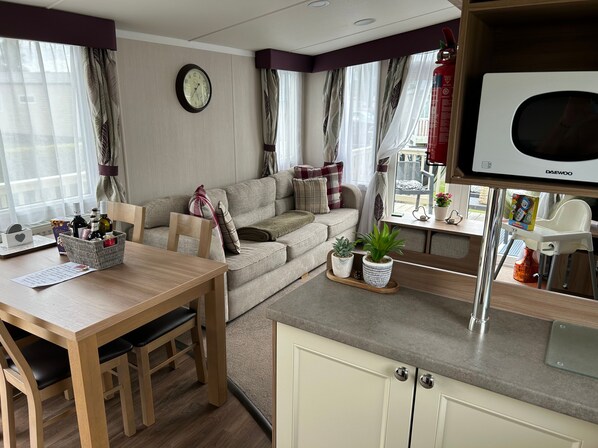 A cozy living area with a sofa, a dining table, and a kitchen area with a microwave. - 8 Berth Luxury Caravan On Butlins, Skegness D/F (Skegness)