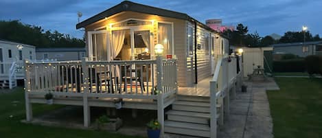 Una casa móvil con terraza, mobiliario exterior y un pequeño jardín.