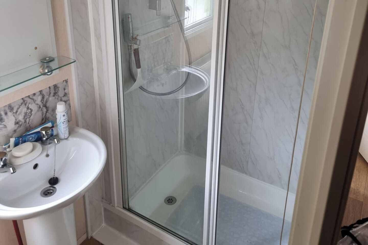 A bathroom with a glass-enclosed shower, a white sink, and a marble backsplash.