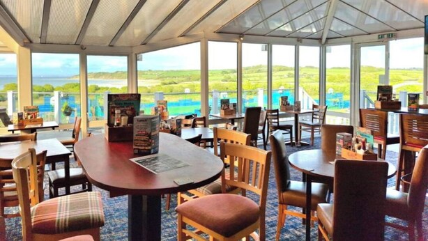 Un restaurante con mesas y sillas, un atril para el menú y vistas al mar.
