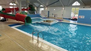 Una piscina interior con tobogán de agua, plataforma de salto y puesto de salvavidas.