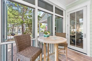 A covered porch with wicker furniture, a round wooden table, and large windows.