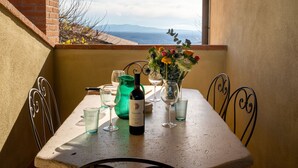 Uma mesa na varanda com uma garrafa de vinho, copos e um vaso de flores.