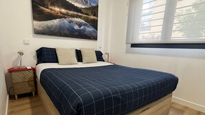 A bedroom with a bed, a nightstand, a wall-mounted air conditioner, a window, and a large landscape painting.