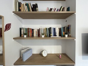 Ein Bücherregal mit Büchern, ein kleiner Topfpflanze, eine Uhr und eine Notizzbox.