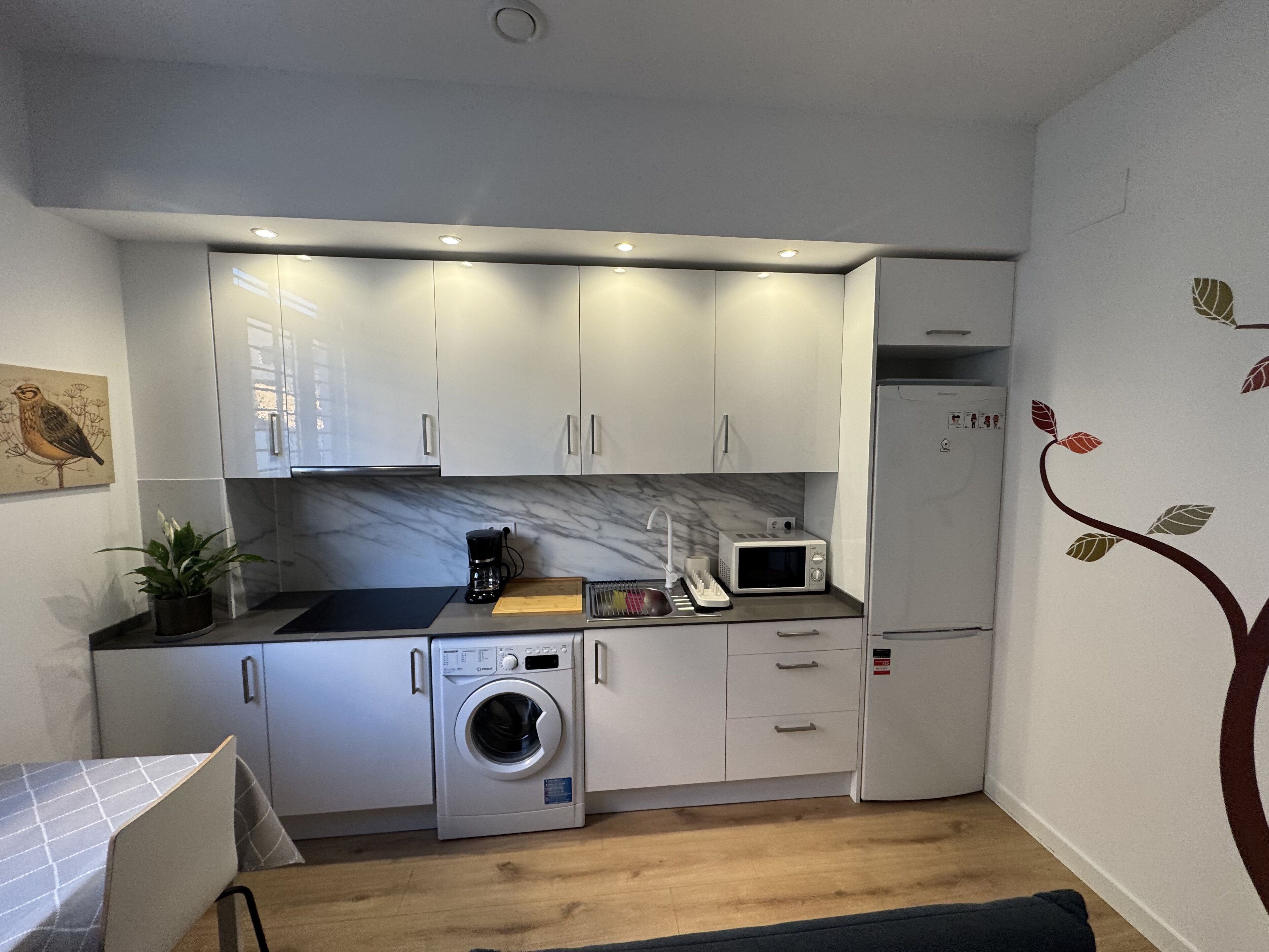 Una cocina compacta con armarios blancos, microondas, lavadora y un lavamanos pequeño.