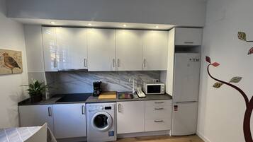 Una cocina compacta con armarios blancos, microondas, lavadora y un lavamanos pequeño.