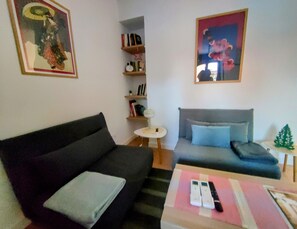 Ein Wohnzimmer mit einer schwarzen Couch, einem grauen Sofa, einem kleinen runden Tisch und einem Bücherregal.