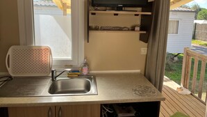 A kitchenette with a sink, a window, a television, and a wooden deck outside. - Mobile Home 'Chez Sylvie' with Shared Pool, Wi-Fi, and Air Conditioning (Argelès-sur-Mer)
