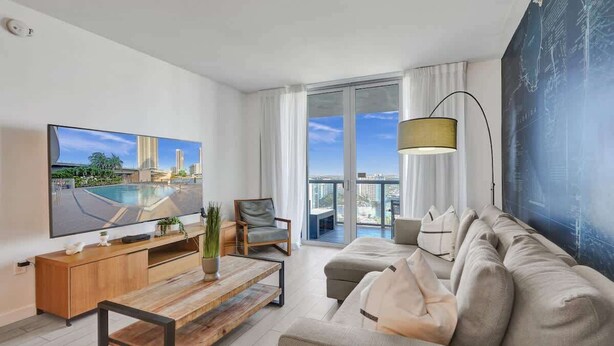 A modern living room with a large flat-screen TV, a sofa, a coffee table, and a chair. - Bay View Fitness Center 1BDR Resort Beach Pool Gym (Hallandale Beach)