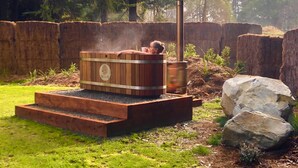 Eine Sauna mit Holzfassade, einem Metallschornstein und einem Steinfundament.