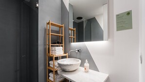 A modern bathroom with a wooden shelf holding towels, a marble sink, and a mirror. - GuestReady - Mompilher Apartments - D (Porto)