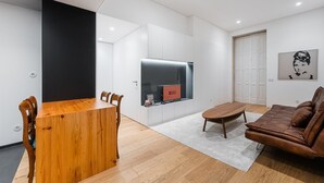 A modern living room with a wooden dining table, a brown leather sofa, and a flat-screen TV mounted on a white wall. - GuestReady - Mompilher Apartments - D (Porto)