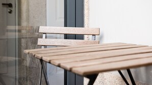 A wooden chair and table in a room with a glass door and a white wall. - GuestReady - Mompilher Apartments - D (Porto)