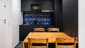 A compact kitchen with a black microwave, a sink, and a blue-tiled backsplash. There is a wooden dining table with four chairs. - GuestReady - Mompilher Apartments - D (Porto)