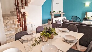 A dining area with a table set for four, a staircase with wooden balusters, a fireplace, and a teal accent wall. - V2 Caliços - VIP Properties by Interhome (Albufeira)