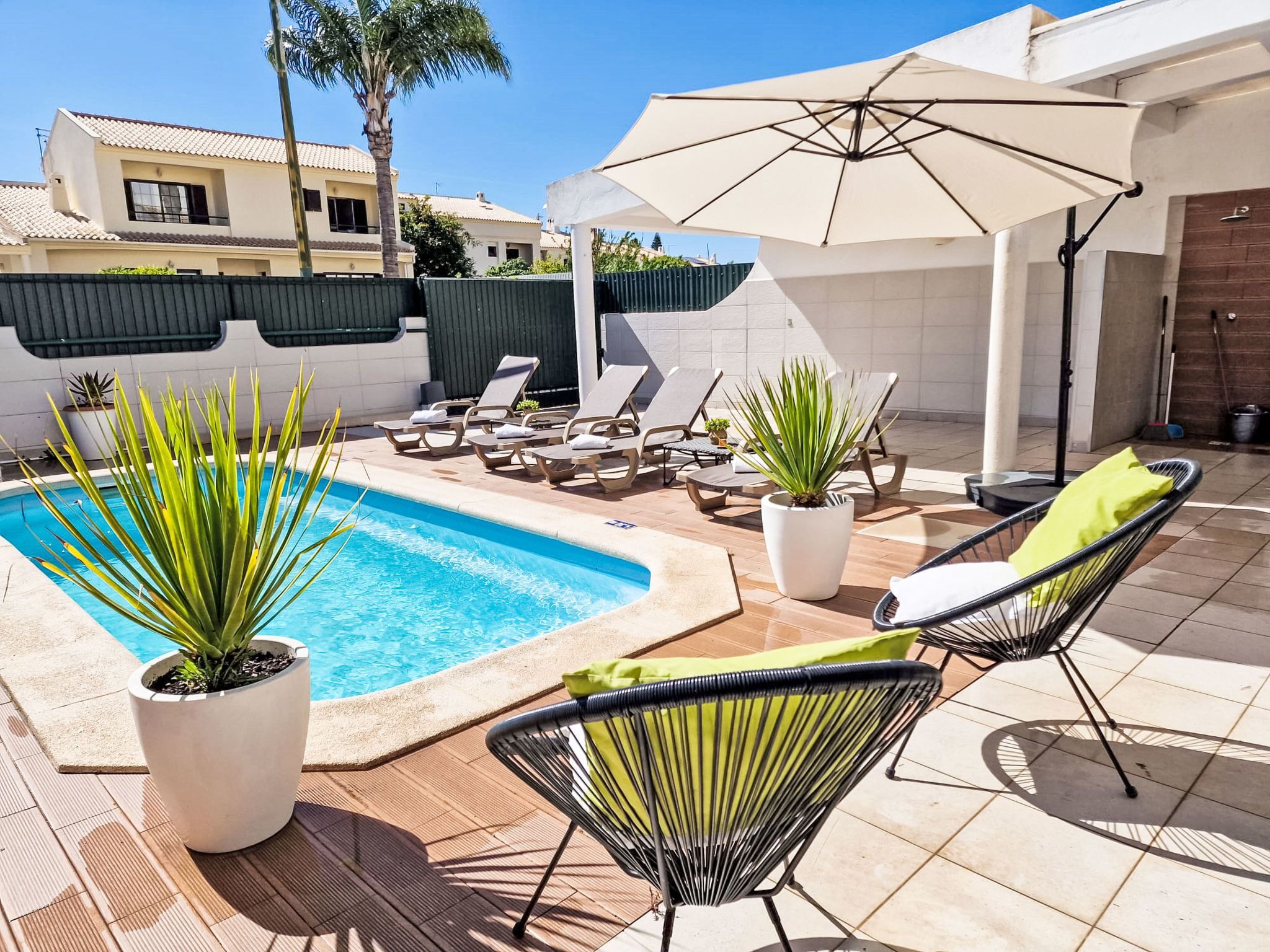 A swimming pool with lounge chairs and umbrellas, surrounded by potted plants and a tiled patio area.
