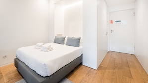 A modern bedroom with a large bed, grey and white pillows, and neatly folded towels. - GuestReady - Mompilher Apartments - C (Porto)