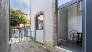 A balcony with a wooden floor, a small table with chairs, and a large window. - GuestReady - Mompilher Apartments - C (Porto)
