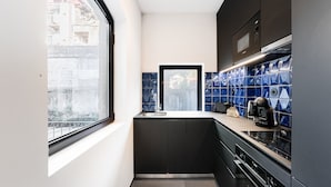 A modern kitchen with black cabinets, a stainless steel sink, and a window overlooking a cityscape. - GuestReady - Mompilher Apartments - C (Porto)