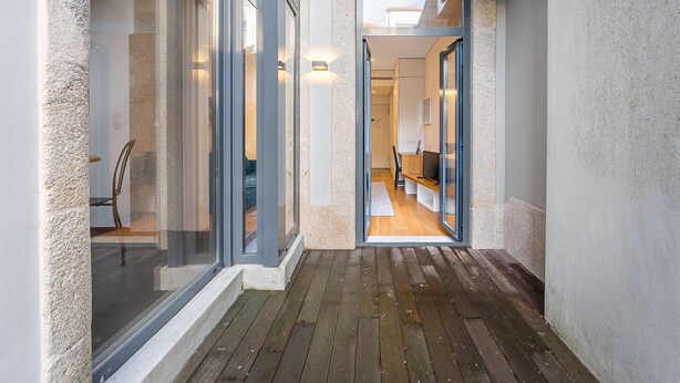 A narrow corridor with wooden flooring leading to a room with a desk and chair, a television, and a white rug. - GuestReady - Mompilher Apartments - C (Porto)