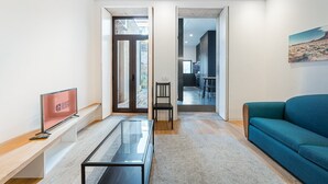 A modern living room with a glass coffee table, a blue sofa, and a TV on a wooden shelf. - GuestReady - Mompilher Apartments - C (Porto)