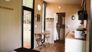 Una cocina compacta con una mesa y sillas de madera, un refrigerador pequeño y una ventana con vistas a árboles.