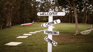 Un cartel direccional con la palabra 'WELCOME' en la parte superior, indicando 'CABIN 1' y 'CABIN 2', y un cartel de 'PARKING' debajo.