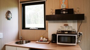 Una cocina compacta con un lavamanos, un microondas, una cafetera y una ventana con vistas a árboles.