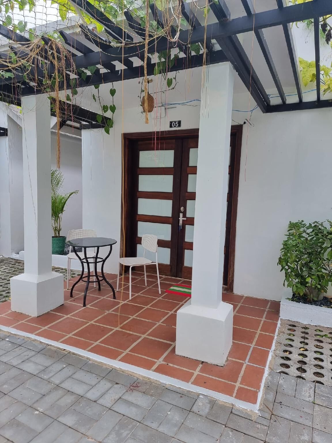 A covered patio area with a tiled floor, a table with two chairs, and potted plants.