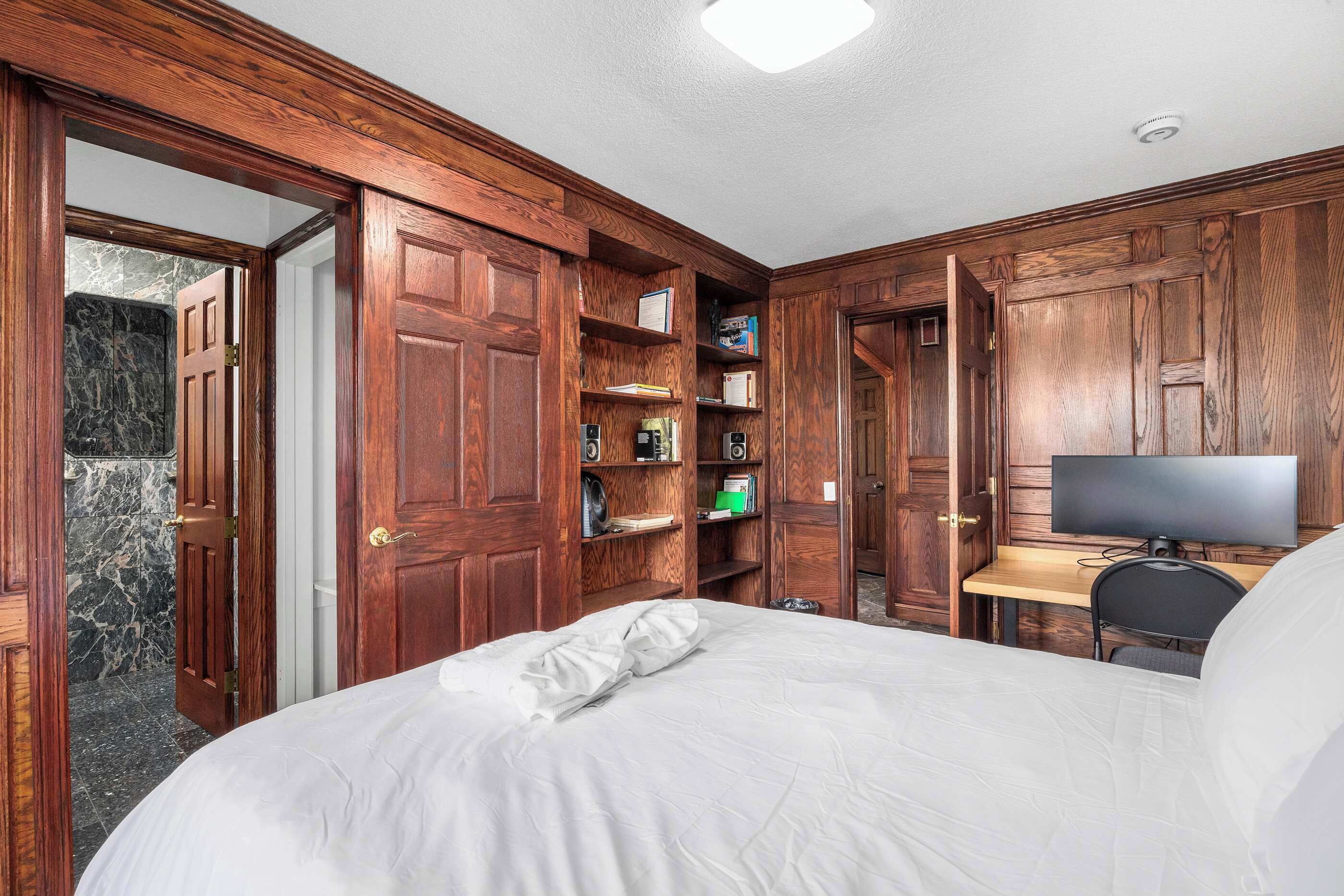 A bedroom with a bed, a desk with a computer, and built-in wooden shelving.